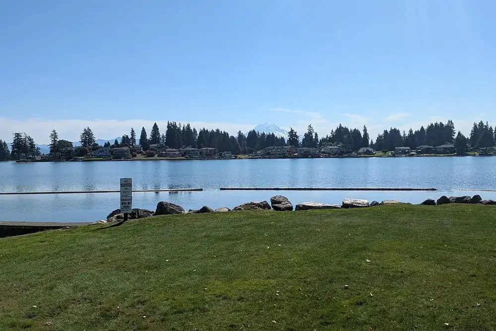 Calm water and tree-lined shore of Lake Tapps from a lawn in Lake Tapps, Washington