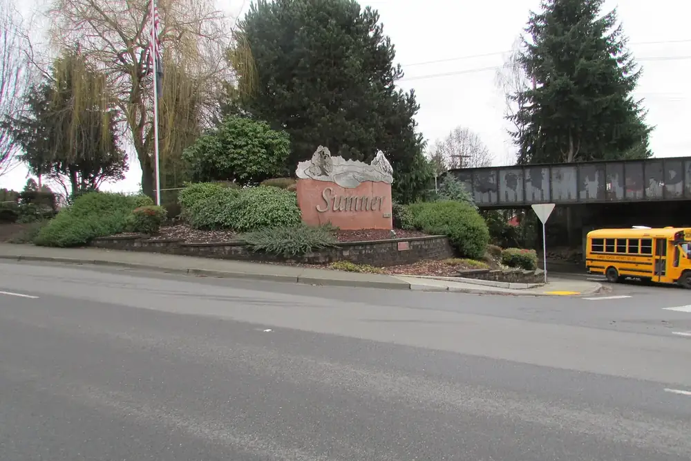 Sumner entrance monument among shrubs beside a road and a rail bridge in Sumner, Washington